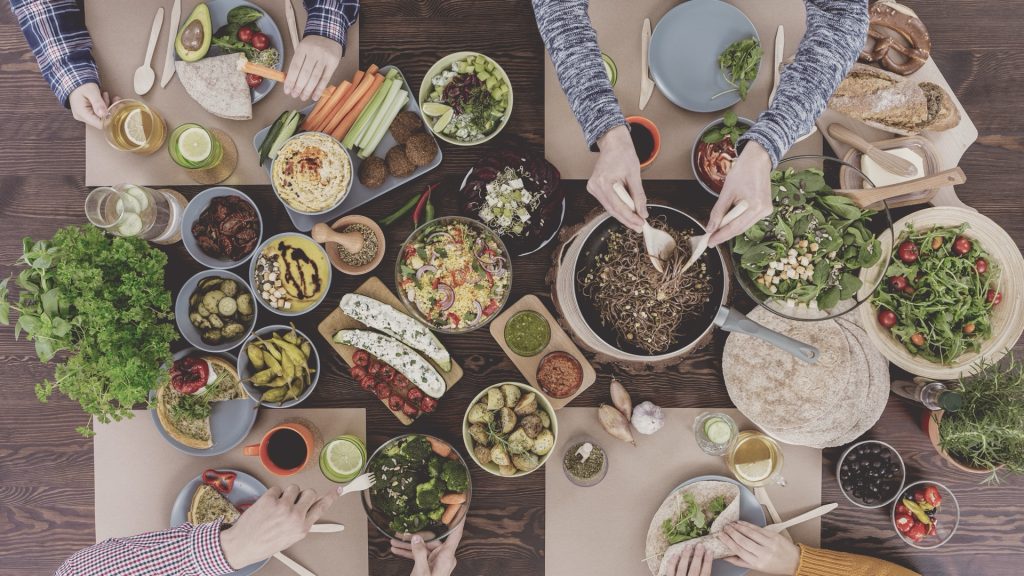 Vue aérienne d’une table composée de plats végétaux et de convives