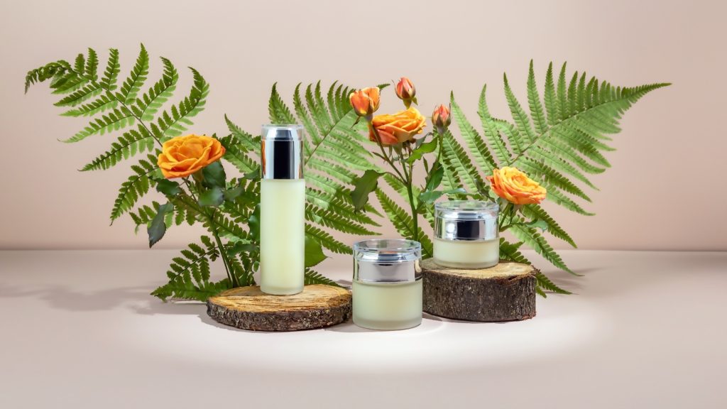 Flacons et pots de cosmétiques entourés de feuillage et de roses
